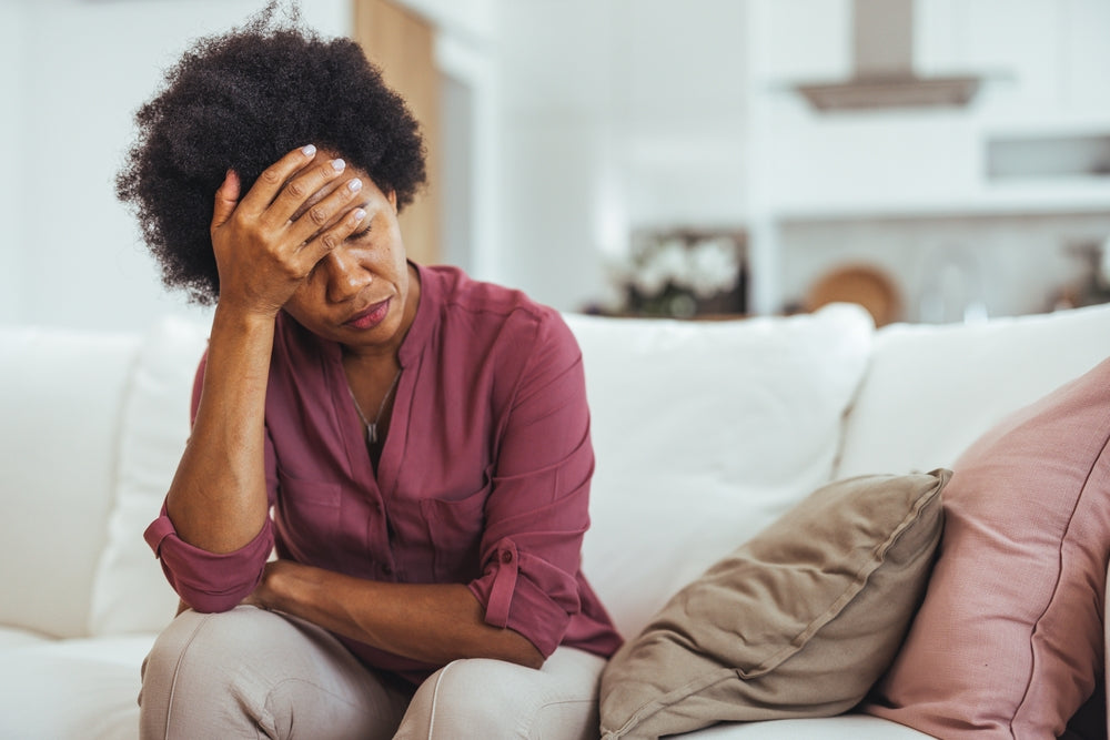 A stressed middle aged woman sitting on the sofa with her head in her hand