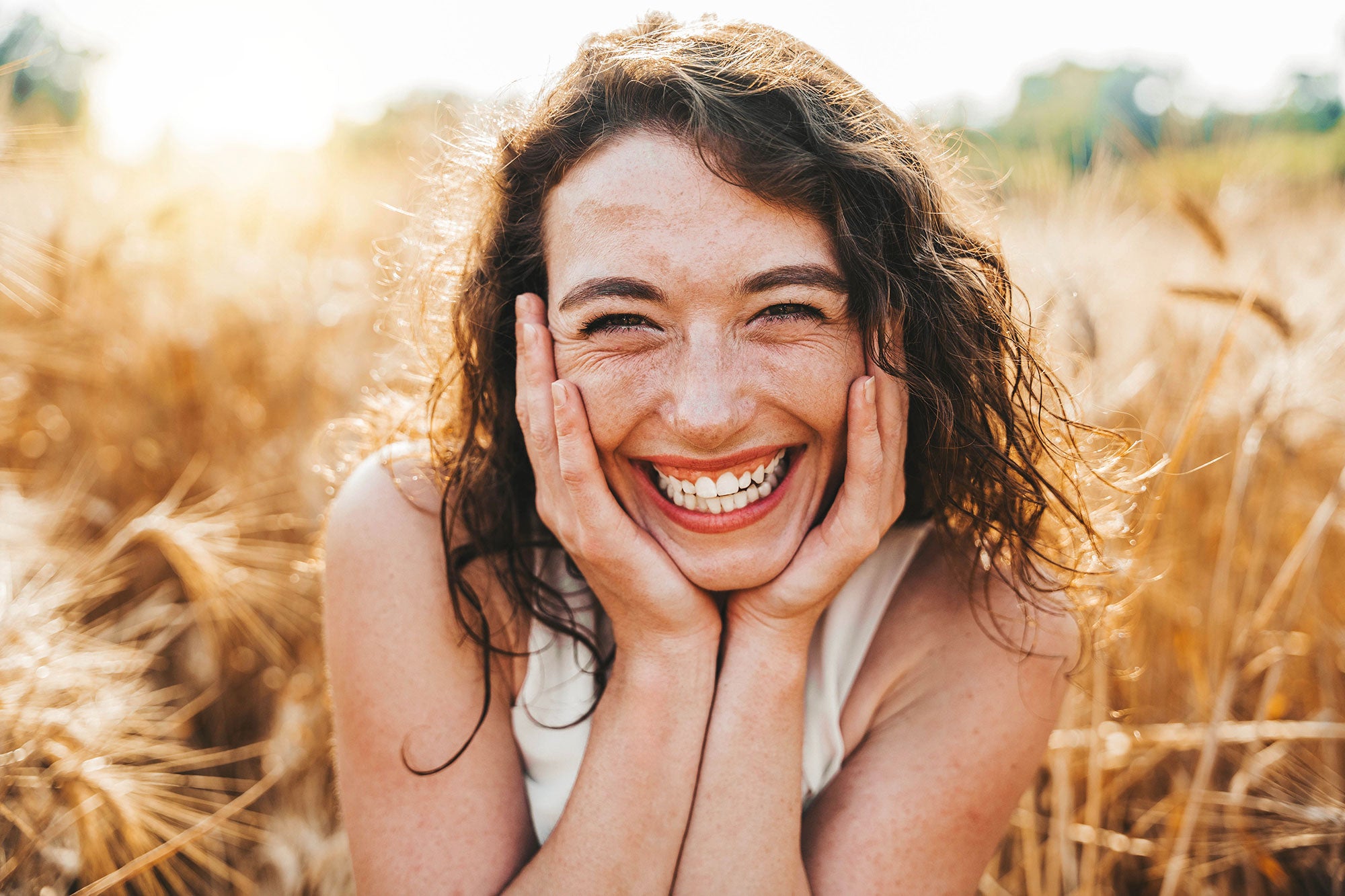 Woman laughing with hands on face in a field of tall grass