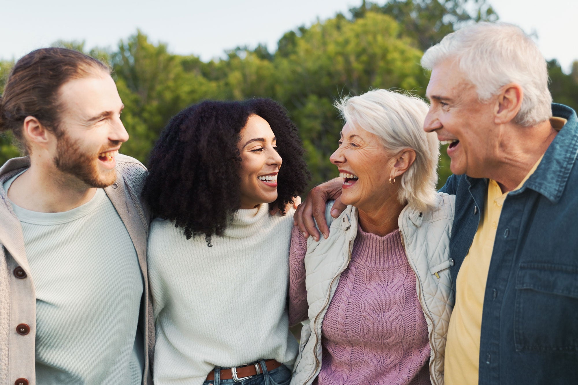 Four people laughing together outdoors with trees in the background