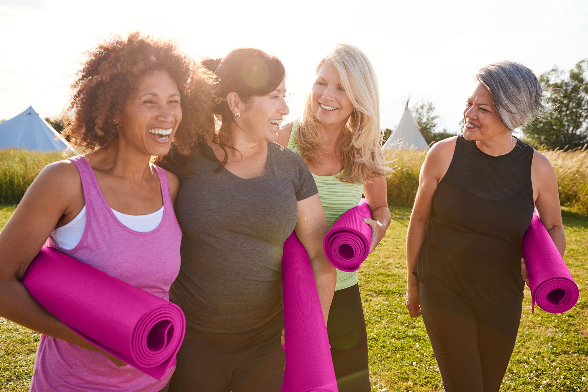 Four women with yoga mats walking outdoors in a grassy area.
